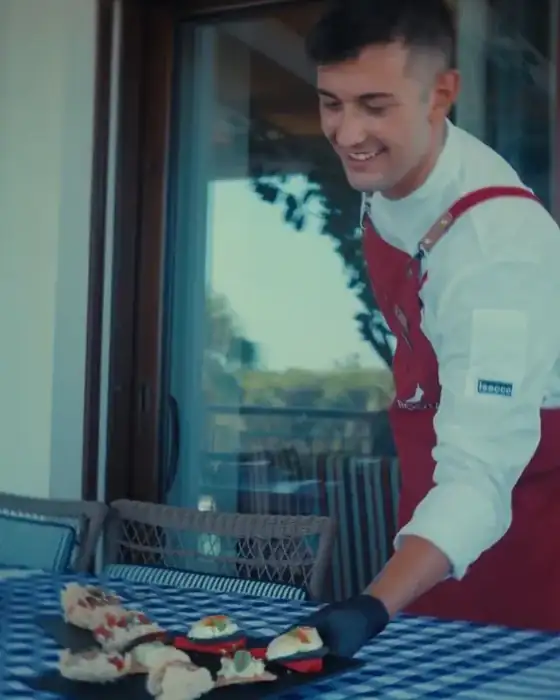 Roota chef smiling as he serves a plate of appetizers on a gingham-covered table