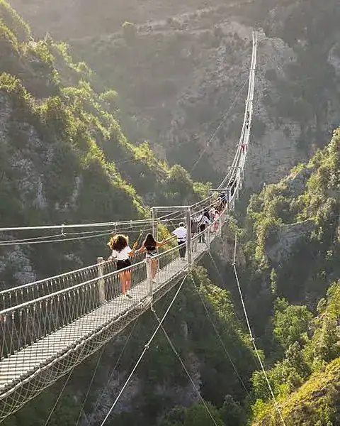 Visitors crossing the Tibetan bridge of Castelsaraceno above a green gorge